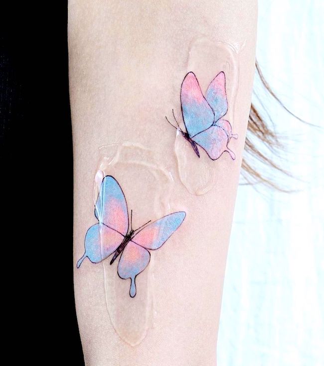 Blue and pink butterflies on the arm by @tattooist_color.b