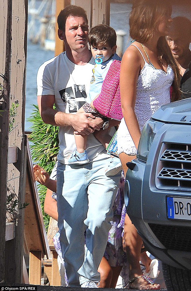 Proud papa: Lionel holds his son as he stands beside his glamorous girlfriend Antonella Roccuzzo