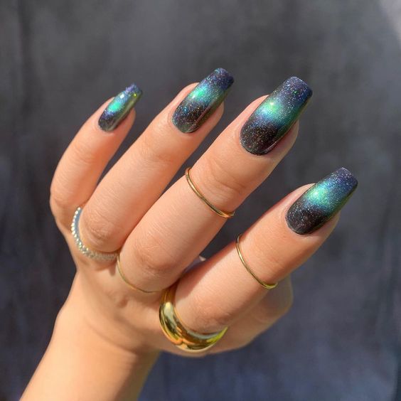 Combination of black and green galaxy-inspired nail art on long tapered square nails