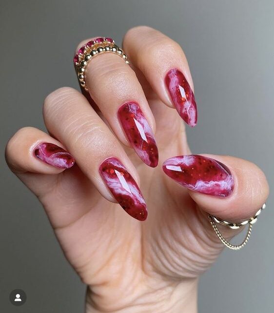 Red and pink marbled galaxy nail art in glossy finish on long almond shaped acrylic nails