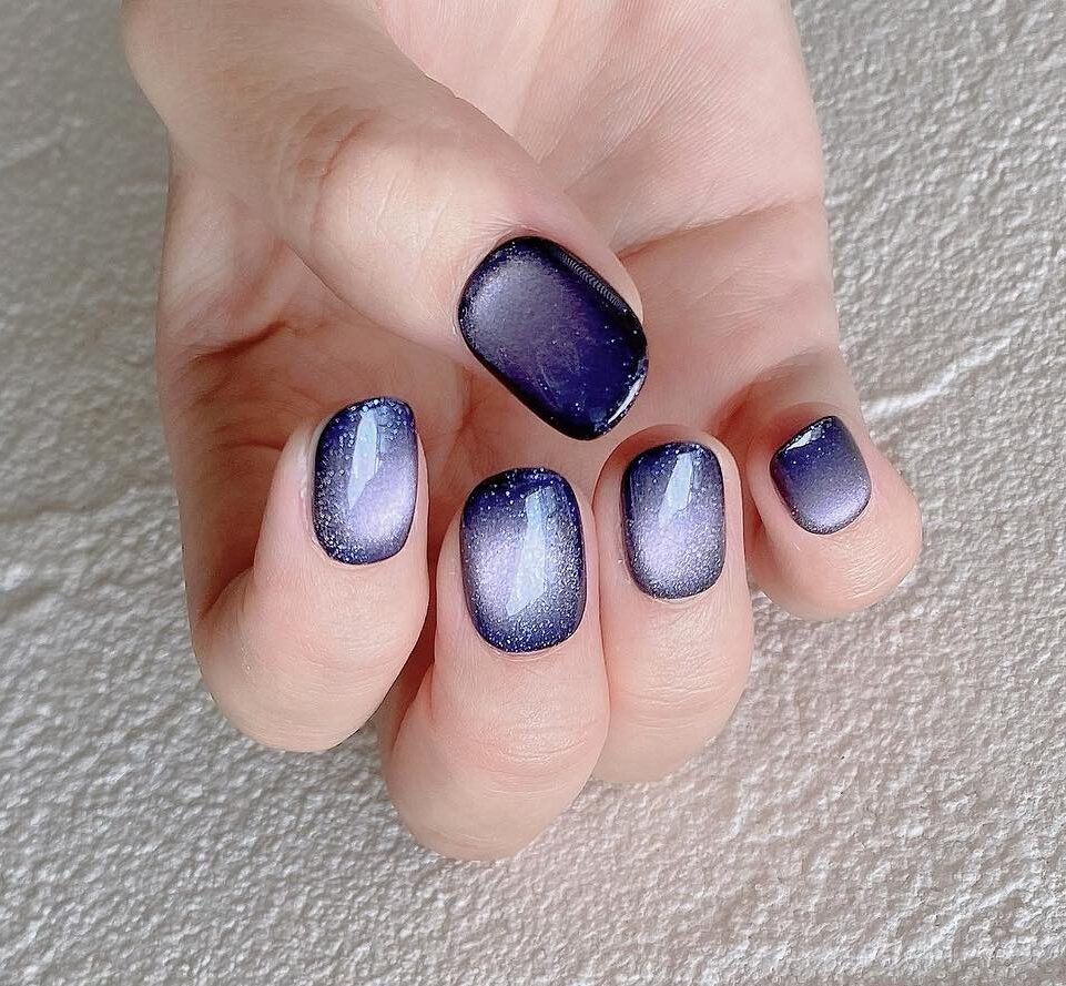 Holographic blue galaxy-inspired nail art on short round nails