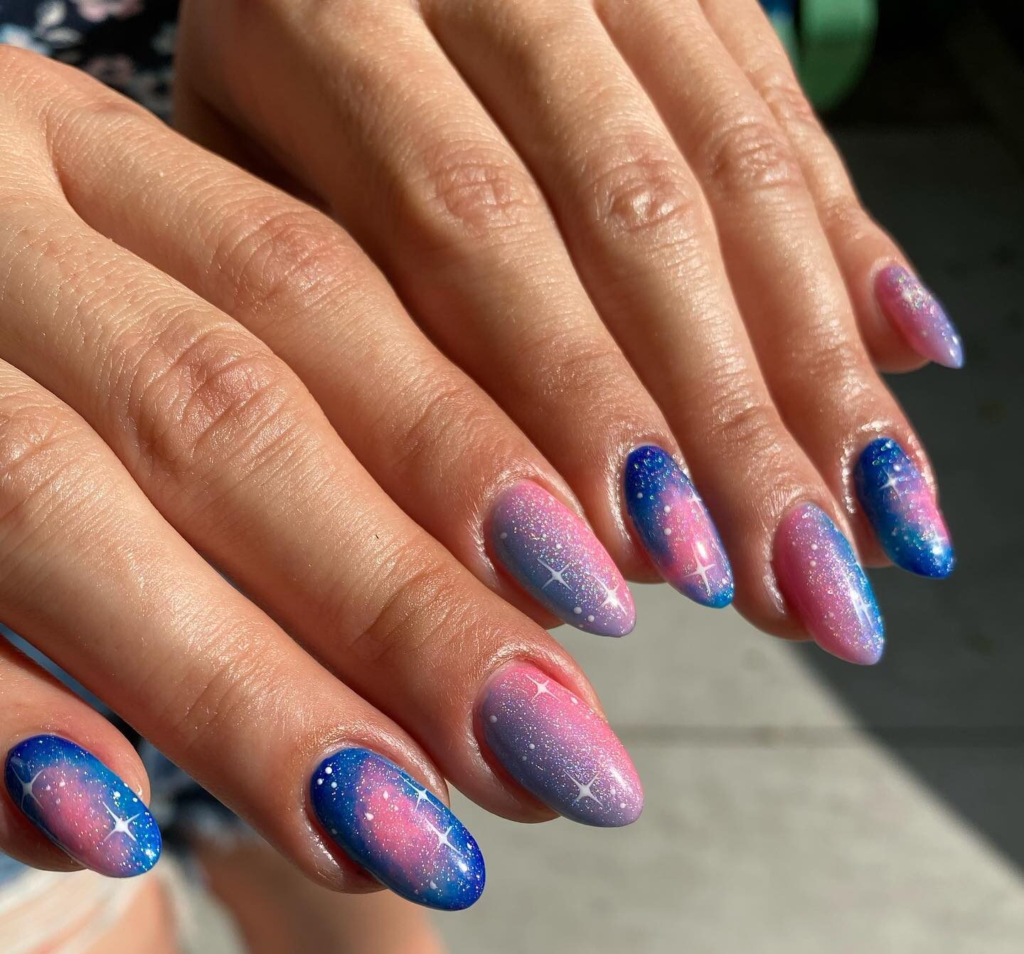 Light pink and blue nail colors with glittery galaxy-themed nail art on medium round nails