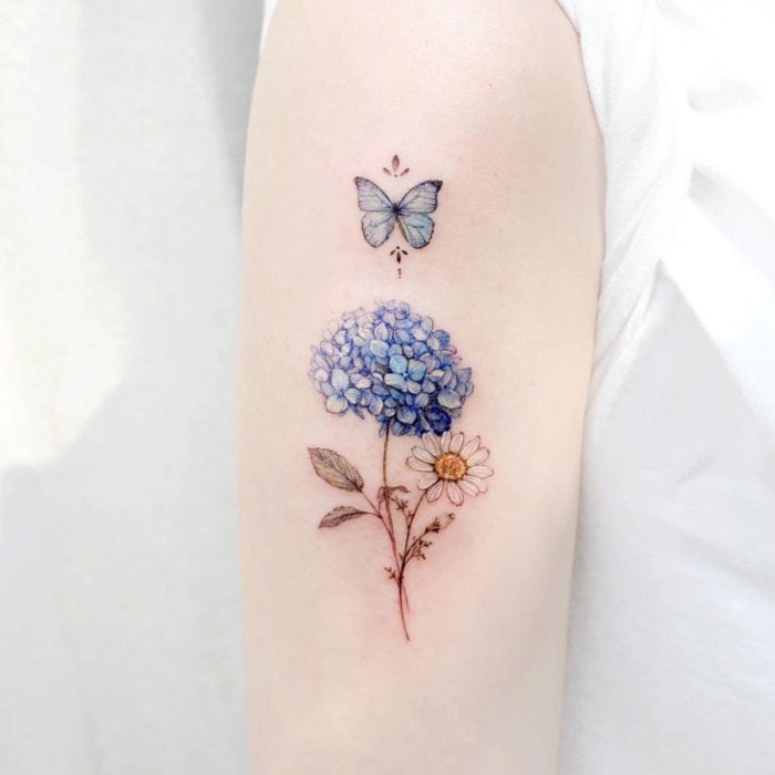 Mini, small tattoo of feminine blue hydrangea flowers and white daisy with butterfly on the arm