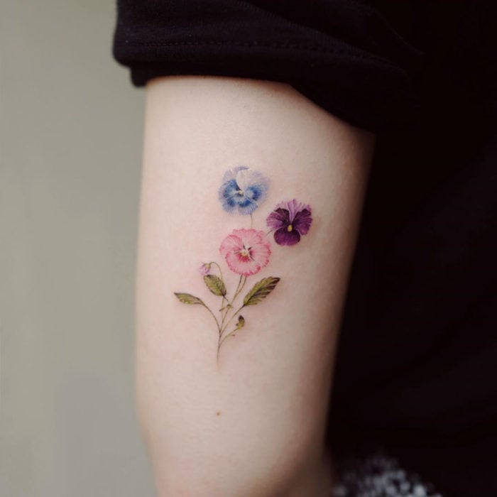 Mini, small tattoo of feminine blue, pink and purple pansy flowers on the arm, triceps