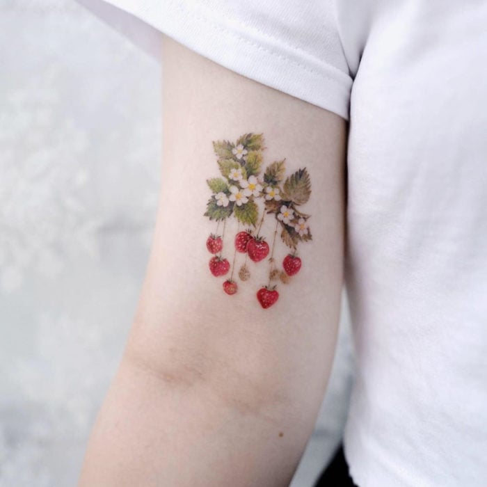 Mini, small tattoo of female strawberry flowers on the arm, bicep