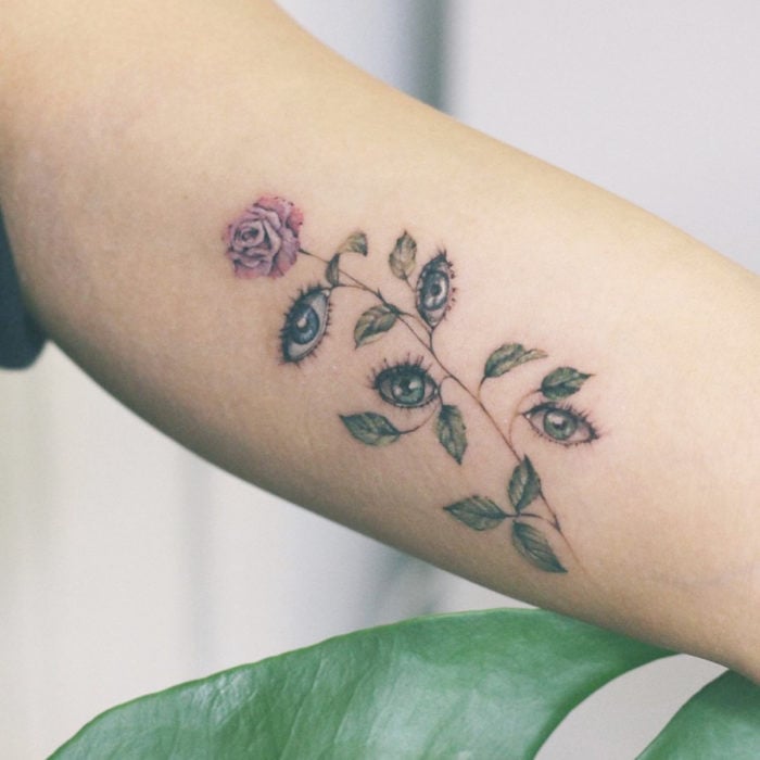 Mini, small tattoo of feminine rose flowers with eyes instead of leaves, on the arm